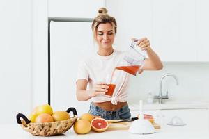 donna scrosciante appena spremuto fatti in casa pompelmo succo in il bicchiere nel moderno bianca cucina foto