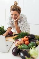 giovane bella donna utilizzando il computer portatile per in linea ricetta ricerca per cucinare a casa foto