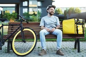 esprimere consegna Corriere seduta su panchina con isolato Borsa e bicicletta. foto