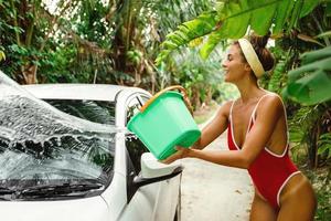 attraente donna con secchio lavaggio sua bianca auto nel Giardino dietro la casa foto