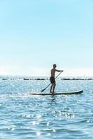 giovane maschio surfer equitazione in piedi paddleboard nel oceano. foto