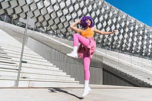 spensierato attivo donna ballerino indossare colorato abbigliamento sportivo avendo divertimento su il strada foto