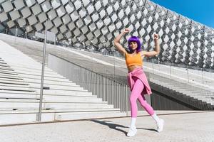 spensierato attivo donna ballerino indossare colorato abbigliamento sportivo avendo divertimento su il strada foto