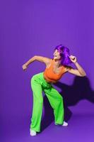 spensierato donna ballerino indossare colorato abbigliamento sportivo avendo divertimento contro viola sfondo foto