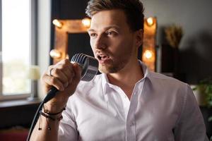 giovane uomo con microfono è cantando a casa foto