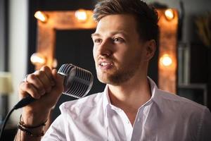 giovane uomo con microfono è cantando a casa foto