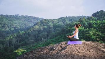 le donne asiatiche si rilassano durante le vacanze. gioca se lo yoga. sulla rupe rocciosa della montagna. natura delle foreste di montagna in thailandia. giovane donna che pratica yoga nella felicità femminile della natura. esercizio di yoga foto
