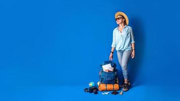 giovane viaggiatore asiatico donna felice in camicia blu con zaino con e attrezzatura per le vacanze dei viaggiatori con una mappa, su sfondo di colore blu. zaino da viaggio foto