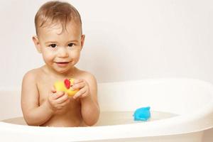 poco ragazzo giocando con gomma da cancellare anatra mentre assunzione un' bagno. foto