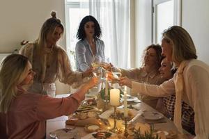 giovane donne amici tintinnante bicchieri a il festivo tavolo. foto