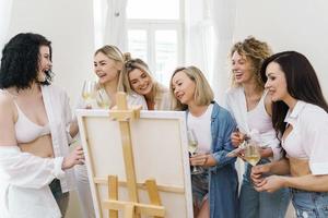 gruppo di donne dipingere su tela e potabile bianca vino durante festa a casa foto