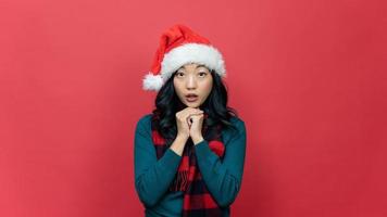 contento bellissimo giovane asiatico donne indossare Santa cappello nel Natale in posa rendere un' desiderio su rosso sfondo. foto