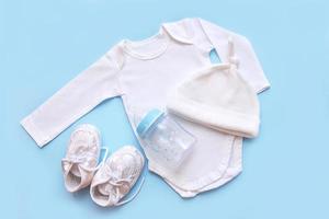 Accessori per un' neonato su un' blu sfondo - berretto, body, stivaletti, latte bottiglia foto