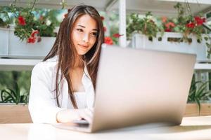 giovane asiatico donna alunno libero professionista con lungo capelli Lavorando su il computer portatile nel strada bar foto