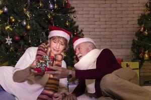 anziano caucasico coppia festeggiare Natale insieme nel felicità e eccitazione a casa con rosso Santa cappello e Natale albero foto