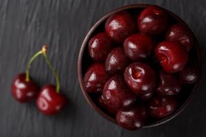 maturo e succoso ciliegia frutti di bosco su un' nero strutturale sfondo nel un' Marrone tazza, con acqua gocce. superiore Visualizza, avvicinamento. foto