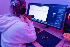 donna blogger utilizzando condensatore microfono durante in linea Podcast nel camera con neon leggero foto