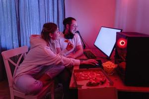coppia chilling a casa nel camera con neon leggero e mangiare Pizza, Guardando film in linea o giocando video Giochi foto