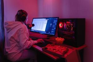 donna gamer o Software sviluppatore seduta a il moderno personale computer e mangiare Rifiuto cibo a notte nel camera con neon luci foto