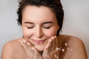 giovane donna lavaggio sua viso con pulito acqua foto