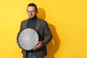 triste uomo indossare bicchieri Tenere grande orologio su giallo sfondo foto