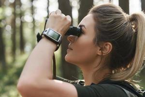 femmina escursionista è utilizzando binocolo per uccello Guardando nel verde foresta foto