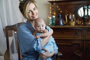 giovane bellissimo madre con sua carino poco bambino avvolto nel il blu stoffa foto