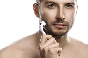 giovane bello uomo è utilizzando derma rullo per barba crescita foto