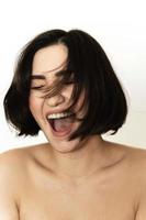 spensierato e contento bruna. giovane donna con volante capelli è ridendo contro bianca sfondo. foto