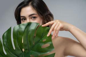 bellissimo donna con un' liscio pelle Tenere verde tropicale foglia su bianca sfondo foto