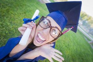 espressive giovane donna Tenere diploma nel berretto e toga foto