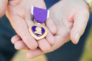 anziano uomo Tenere il militare viola cuore medaglia nel il suo mani. foto