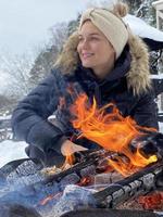 giovane donna riscaldamento su di il fuoco fossa durante freddo inverno giorno foto