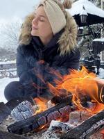 giovane donna riscaldamento su di il fuoco fossa durante freddo inverno giorno foto