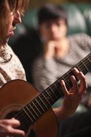 giovane musicista giochi il suo acustico chitarra come amico ascolta foto