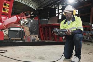 un africano americano produzione ingegnere test e controllo robotica braccio nel meccanico produzione fabbrica, intelligente automatico macchine nel industriale attività commerciale, e futuristico tecnologia innovazione. foto