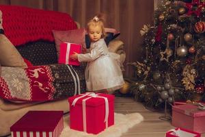 poco bambino ragazza nel vestiti con un' Natale albero a partire dal dietro a foto