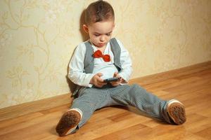 poco ragazzo con cravatta a farfalla giocando mobile Telefono foto
