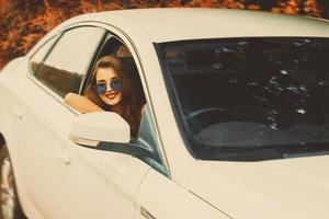 sorridente ragazza nel occhiali da sole essiccazione un' auto foto
