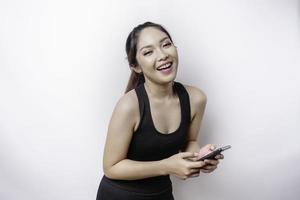 un' ritratto di un' sportivo asiatico donna indossare un' abbigliamento sportivo e Tenere sua Telefono, isolato di bianca sfondo foto