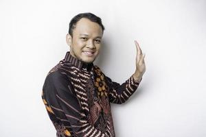 eccitato asiatico uomo indossare batik camicia puntamento a il copia spazio accanto lui, isolato di bianca sfondo foto