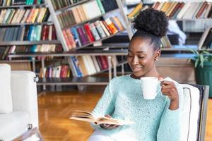 accogliente divano e un' bellissimo ragazza, lettura un' prenotare, concetti di casa e comfort, posto per testo. giovane bella donna seduta e potabile caffè astuzia lettura un' libro gode di riposo foto