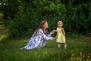 giovane contento elegante giovane madre giochi con sua poco figlia a il verde giardino foto