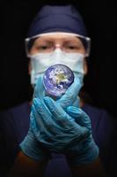 infermiera o medico indossare viso maschera e chirurgico guanti Tenere il pianeta terra foto