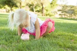 poco ragazza avendo divertimento con sua porcellino banca al di fuori foto