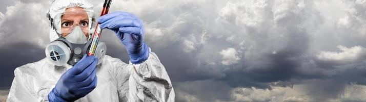 femmina medico o infermiera nel Hazmat Ingranaggio Tenere positivo coronavirus test tubo nuvoloso cielo bandiera foto