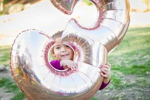 carino bambino ragazza giocando con numero tre mylar Palloncino all'aperto foto