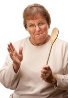 irritato anziano donna con il di legno cucchiaio foto