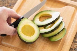 maschio mano prepara fresco tagliare avocado su di legno taglio tavola foto