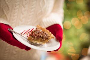 donna indossare rosso guanti Tenere piatto di pecan torta con menta piperita caramella contro decorato albero e luci foto